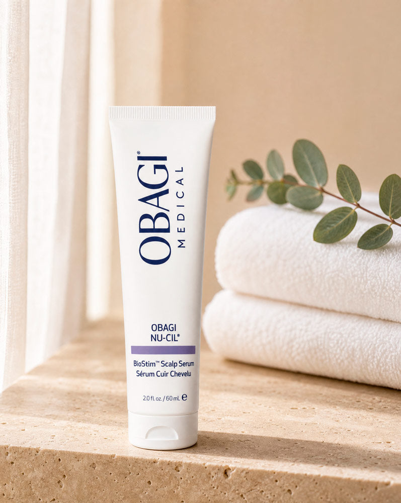 Obagi Nu-Cil BioStim Sérum Capilar de pie sobre repisa de travertino con toallas y eucalipto, vista frontal